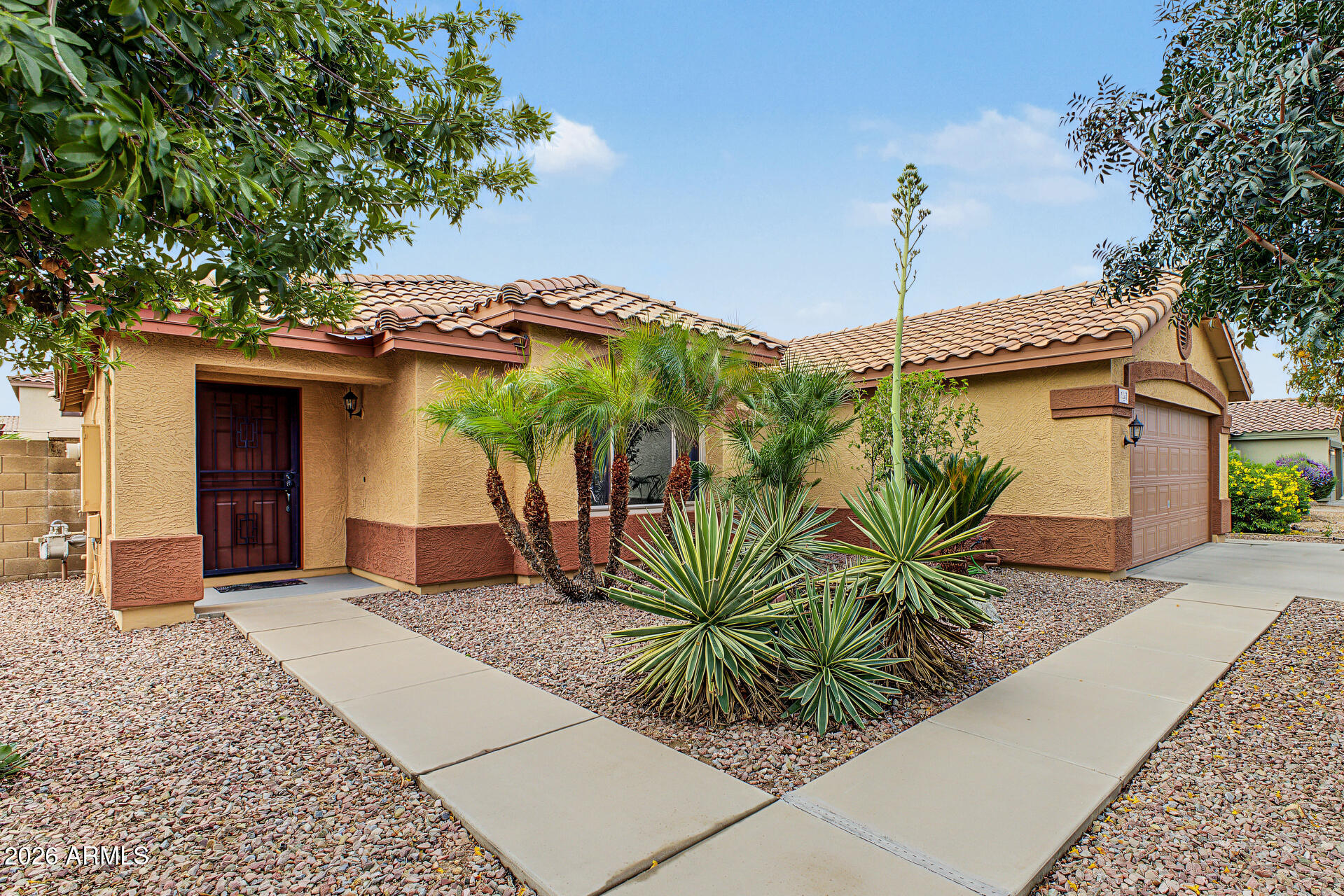 Single-story stucco home with a tile roof, attached garage, and desert landscaping.