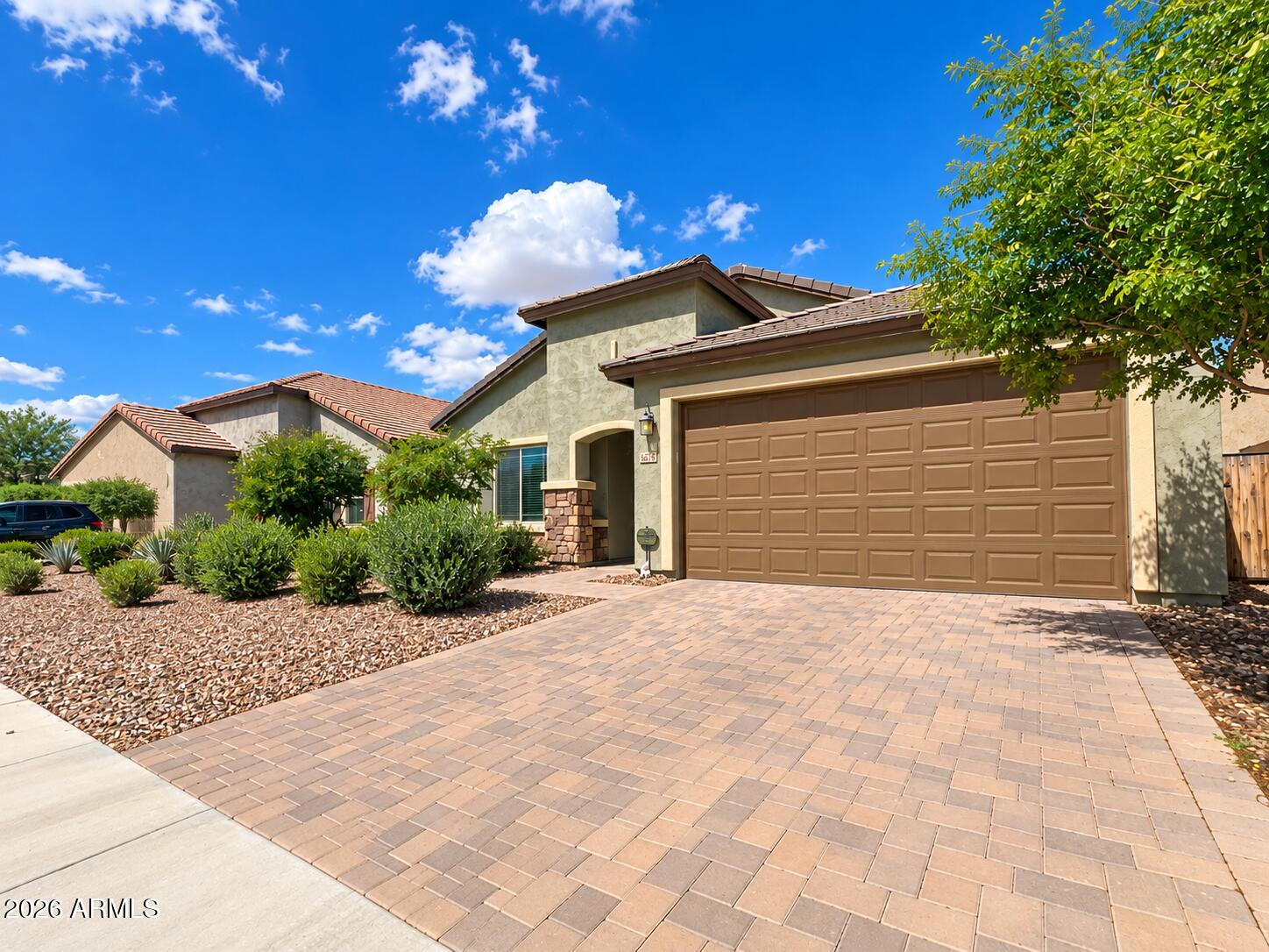Stucco home with a large garage, paver driveway, and desert landscaping.