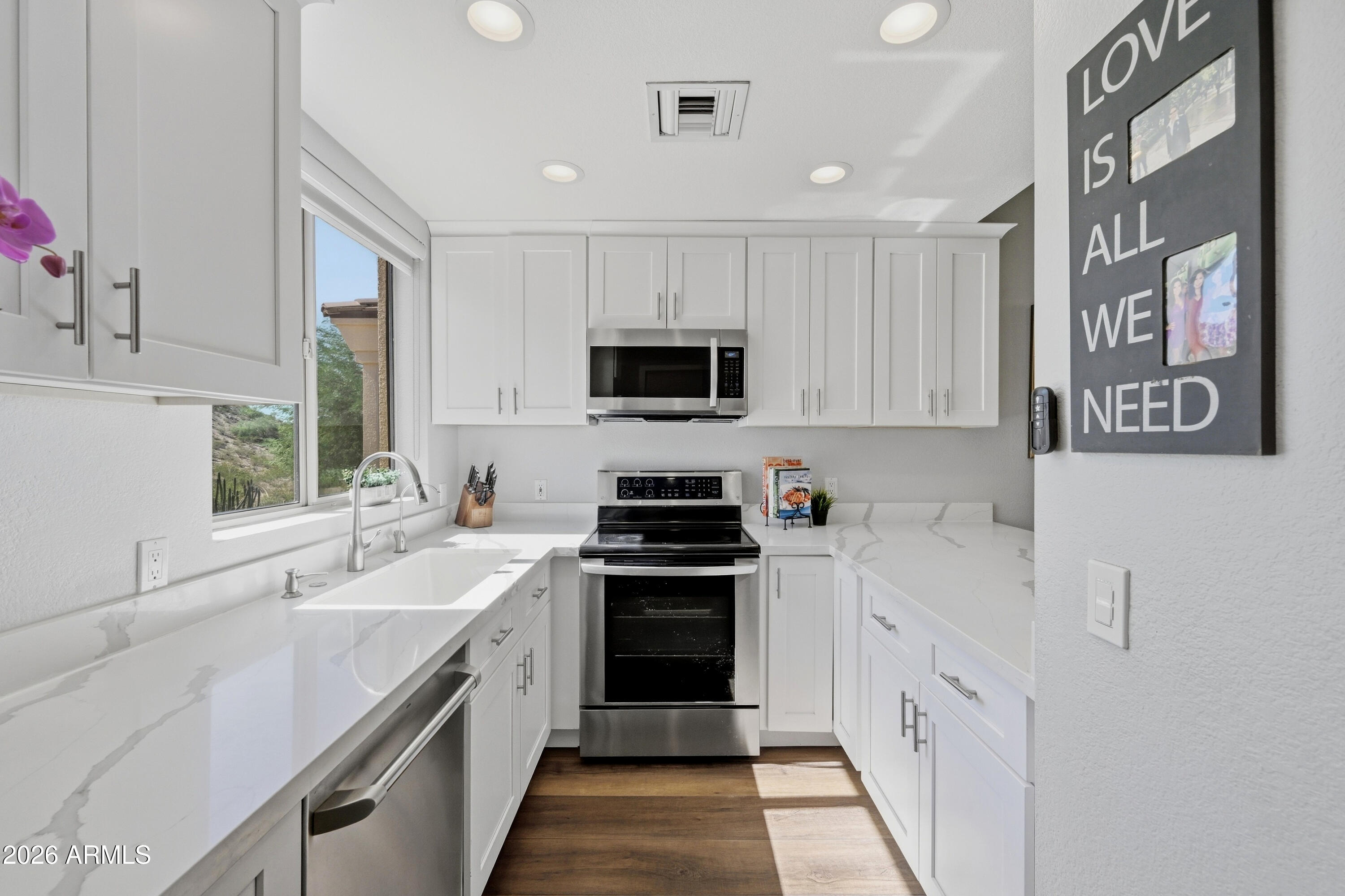 Bright white kitchen with veined countertops, stainless steel appliances, and sunlight through a large window.