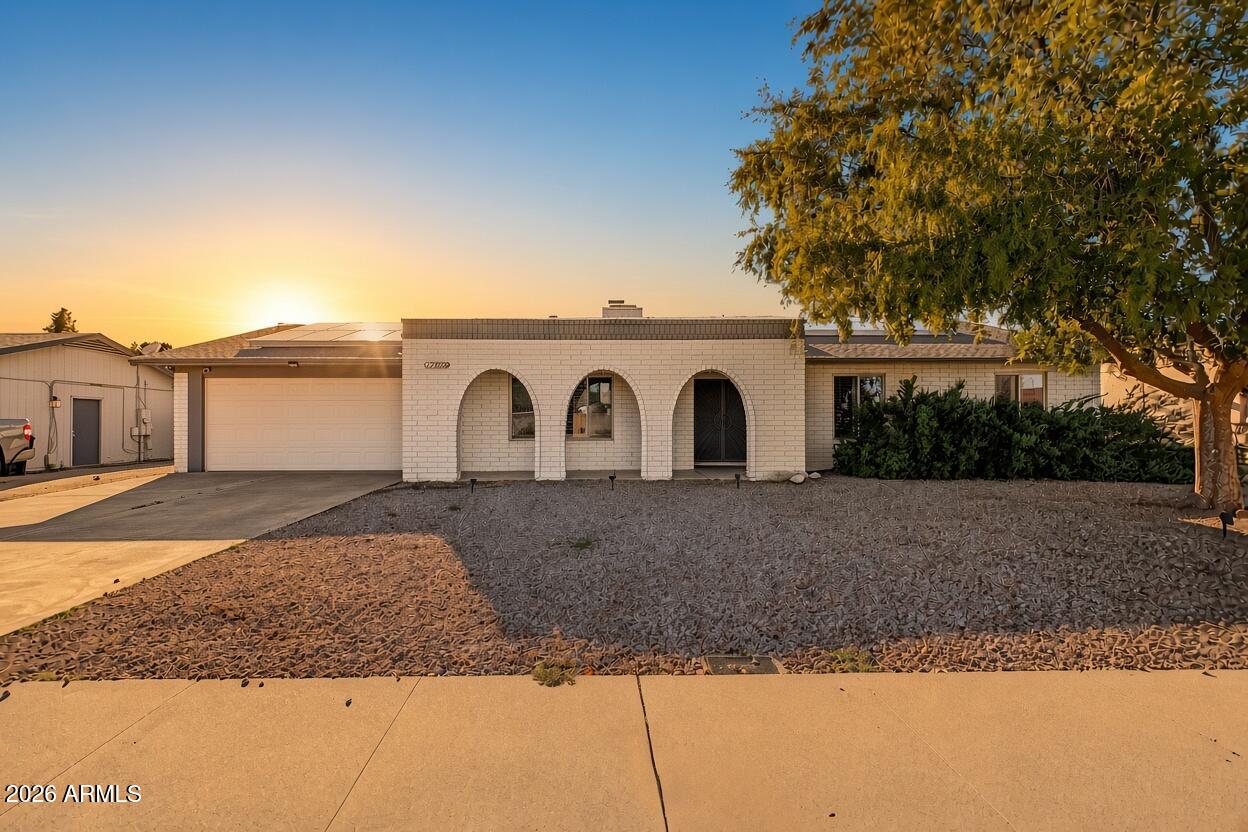 Single-story brick home with arched entry, solar panels, and desert-rock landscaping at sunset.