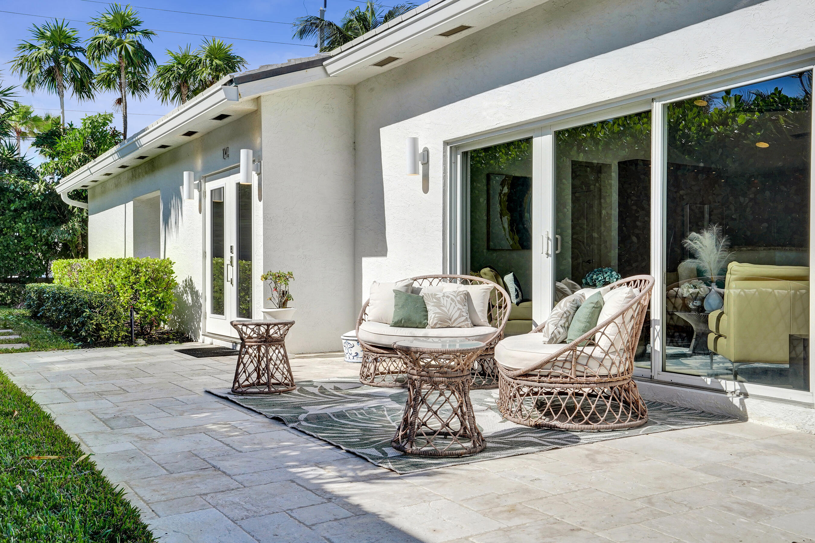 Stone patio with wicker lounge seating beside a modern white stucco home.