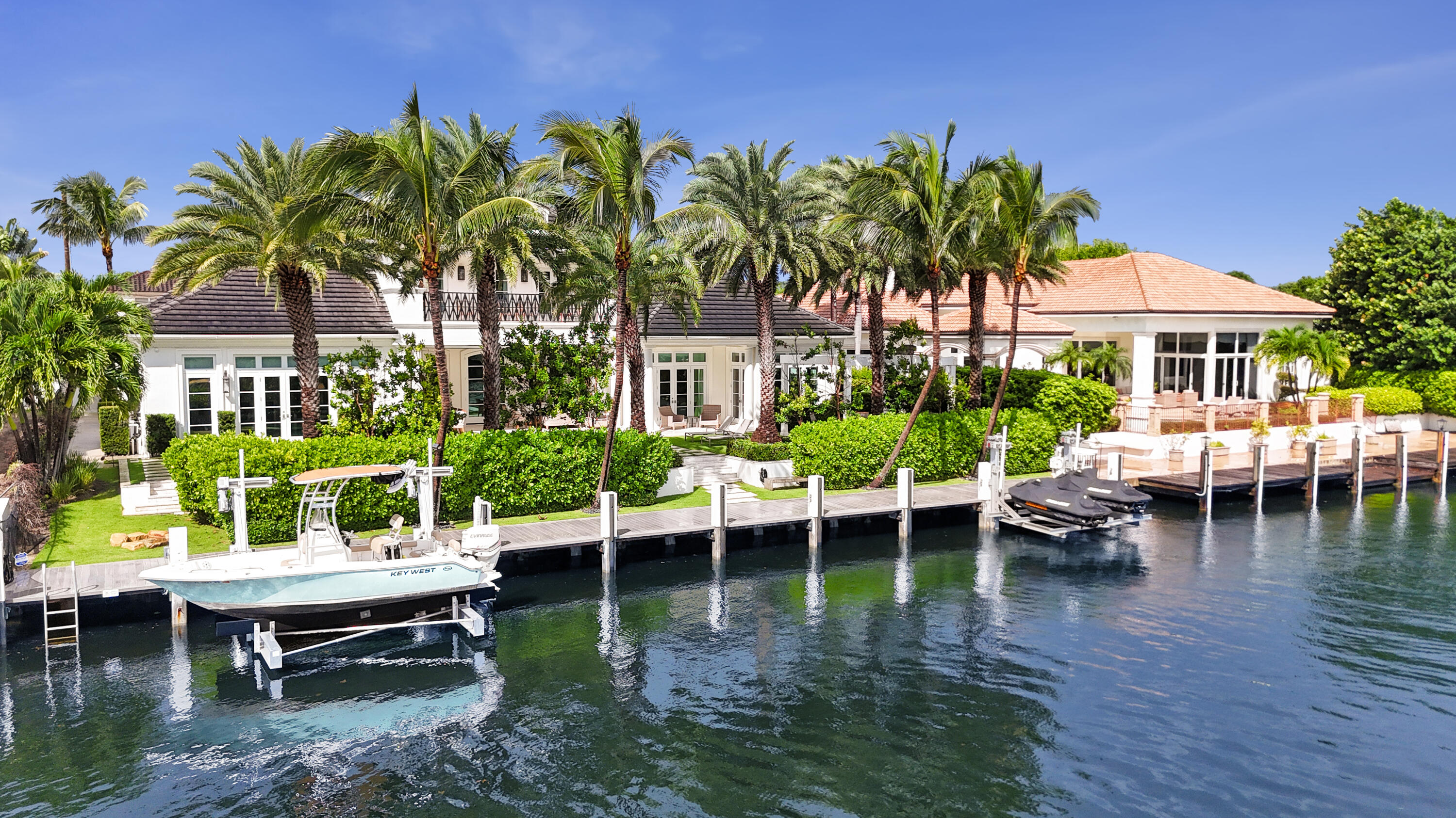 Waterfront home with a palm-lined yard, private dock, and boat on the canal.
