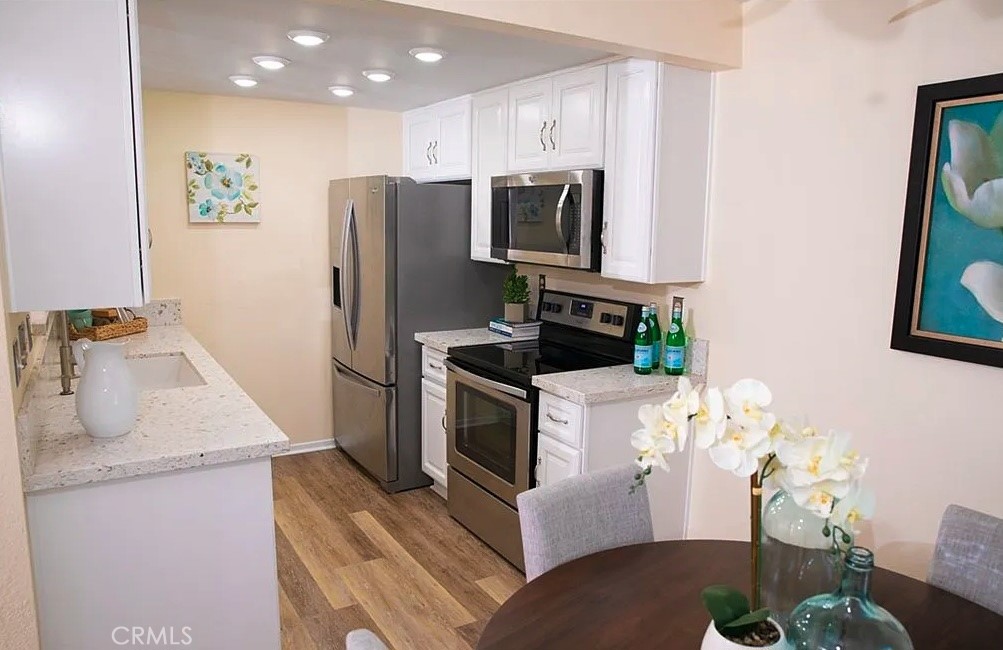 Kitchen with white cabinetry, stainless steel appliances, light countertops, and a dining table with orchids.