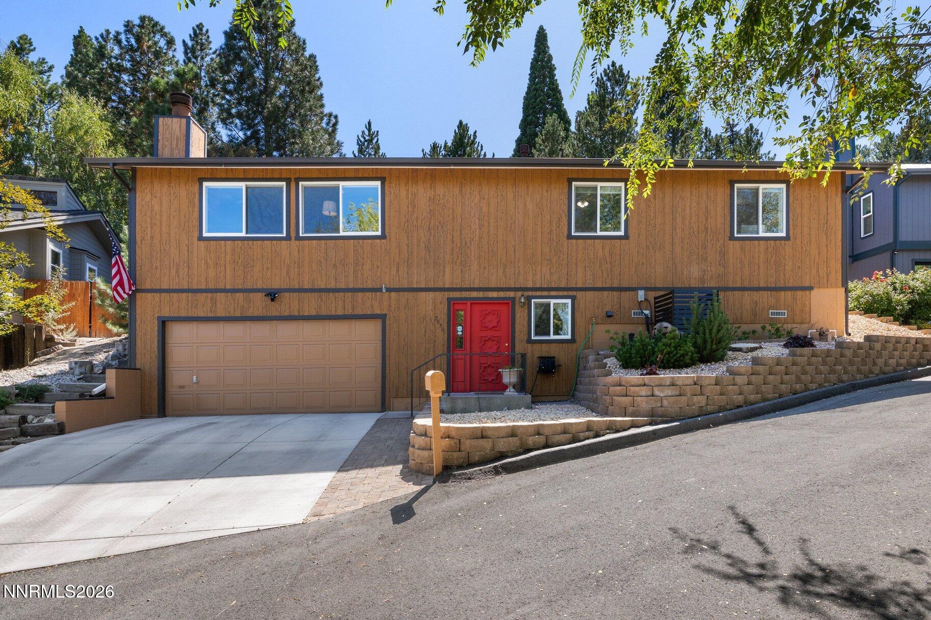 Brown two-story home with a red front door, double garage, and landscaped retaining wall.