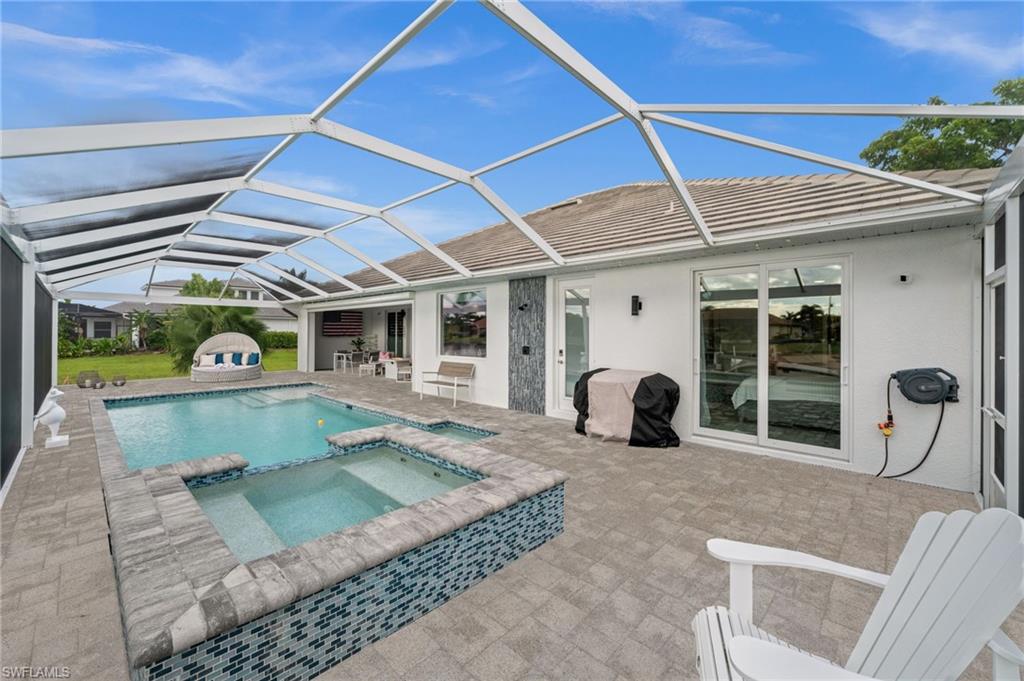 Screened pool lanai with a raised spa, paver patio, and white Adirondack chairs.