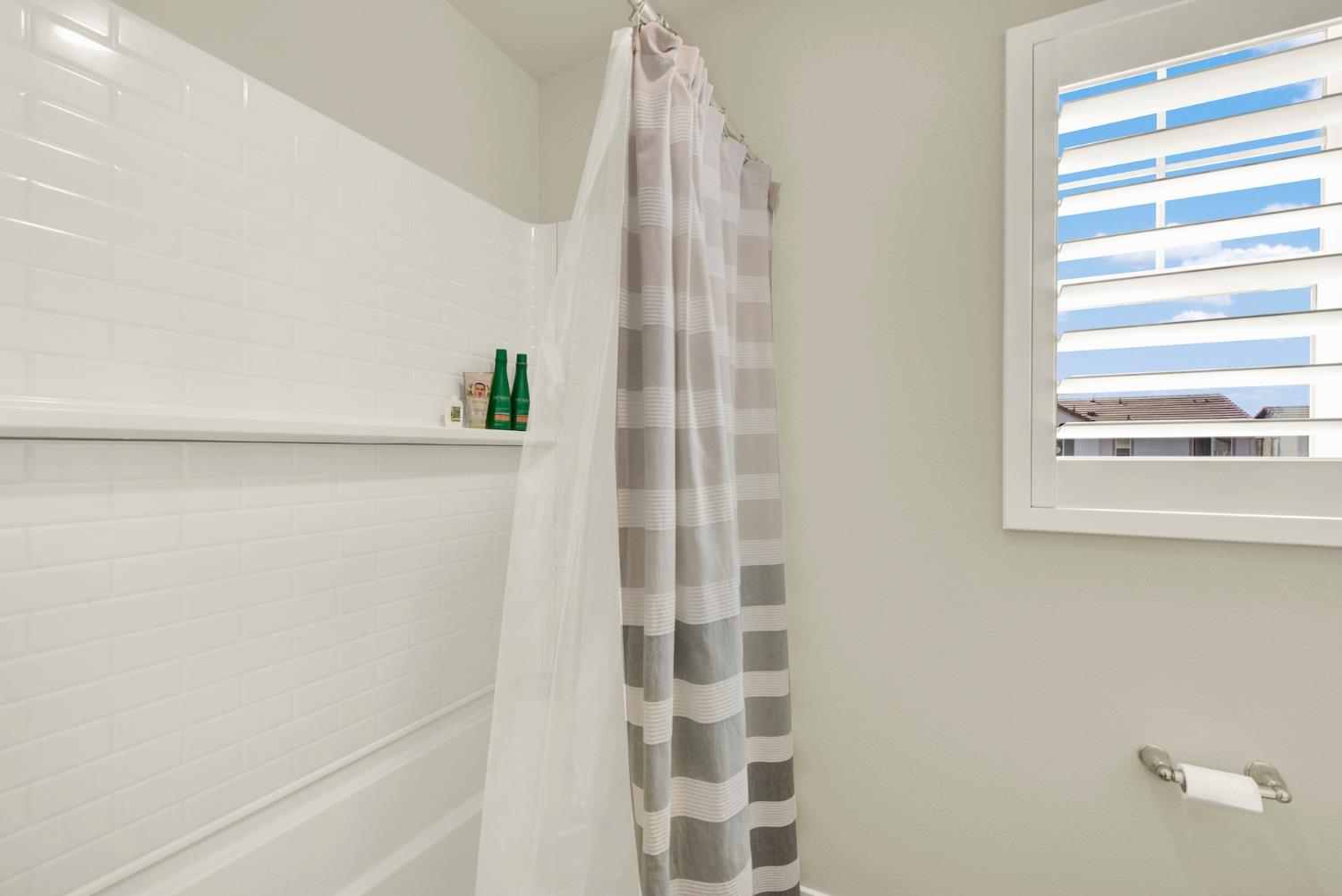 Bathroom with a white subway-tile tub surround, striped shower curtain, and shuttered window.