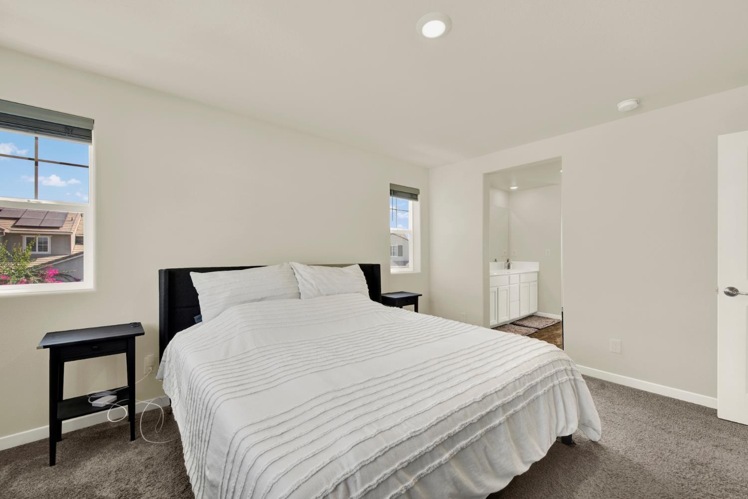 Bedroom with a large white-striped bed, gray carpet, and an open doorway to the en-suite bathroom.