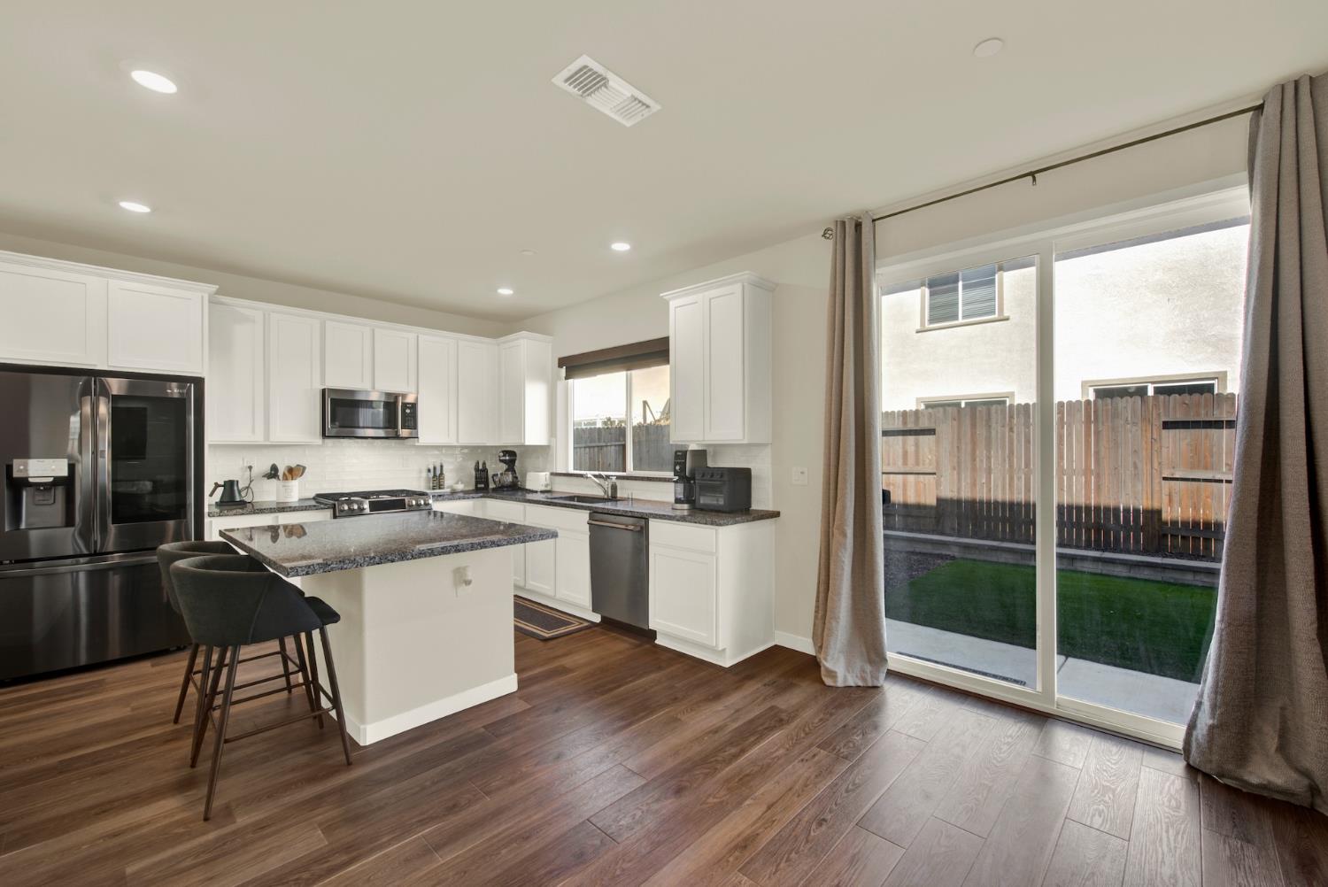 Kitchen with white cabinets, granite counters, stainless appliances, and sliding doors to a fenced backyard.