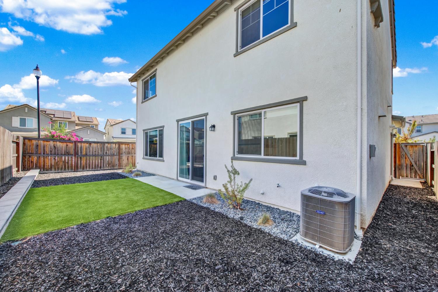 Home’s rear exterior with a fenced yard, artificial turf, gravel landscaping, and a sliding glass door.
