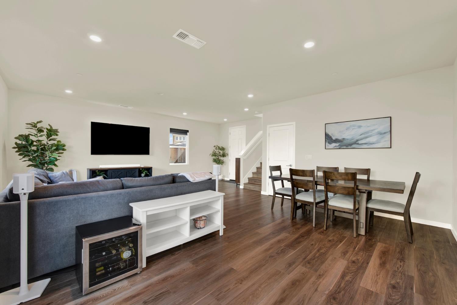 Open-plan living and dining room with dark wood floors, gray sofa, dining table, and staircase.