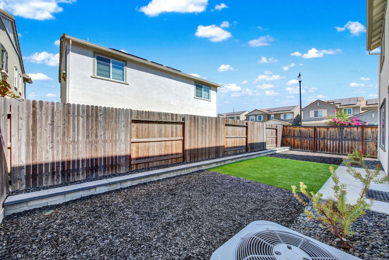 Enclosed backyard with a small lawn, wooden fence, and mulch-and-gravel landscaping.