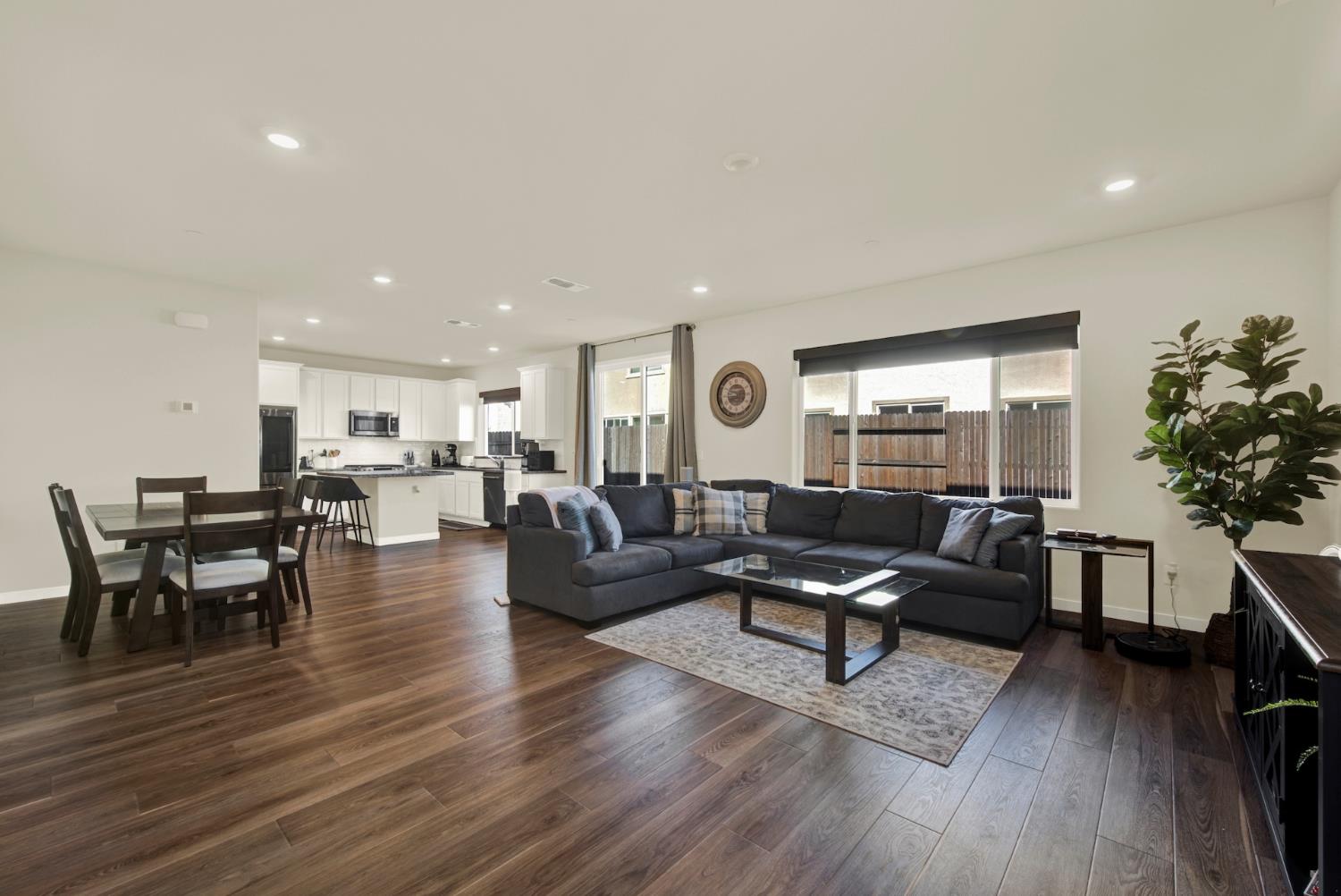 Open-plan living room with a charcoal sectional, dark wood floors, and an adjoining white kitchen.