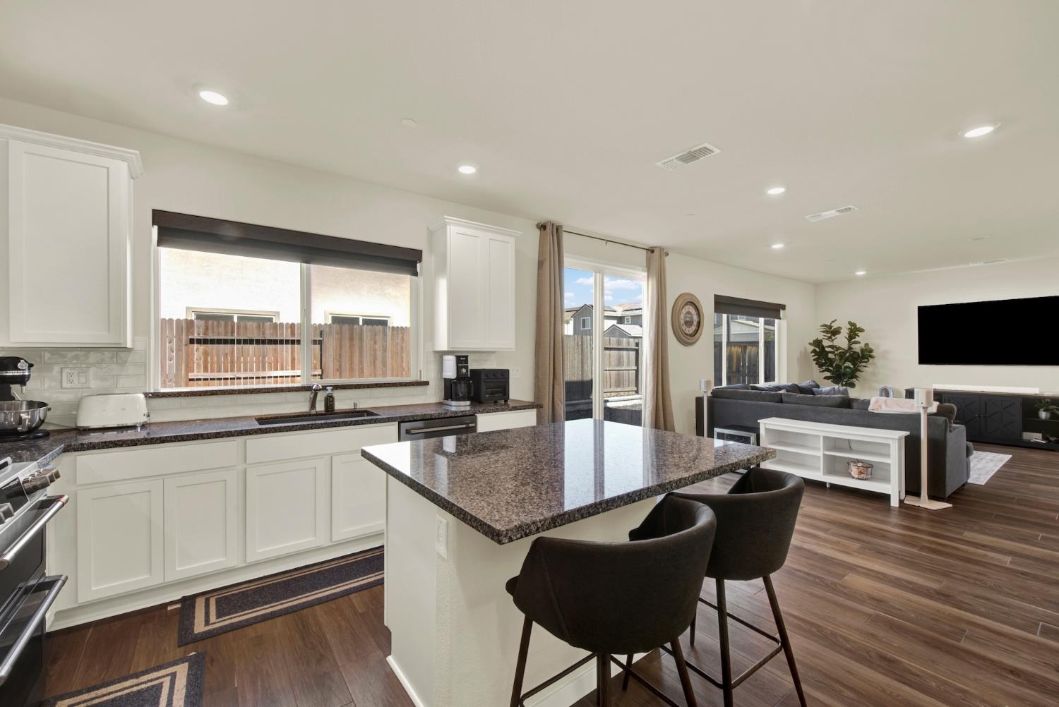 Open kitchen with a granite island and stools adjoining a furnished living room.