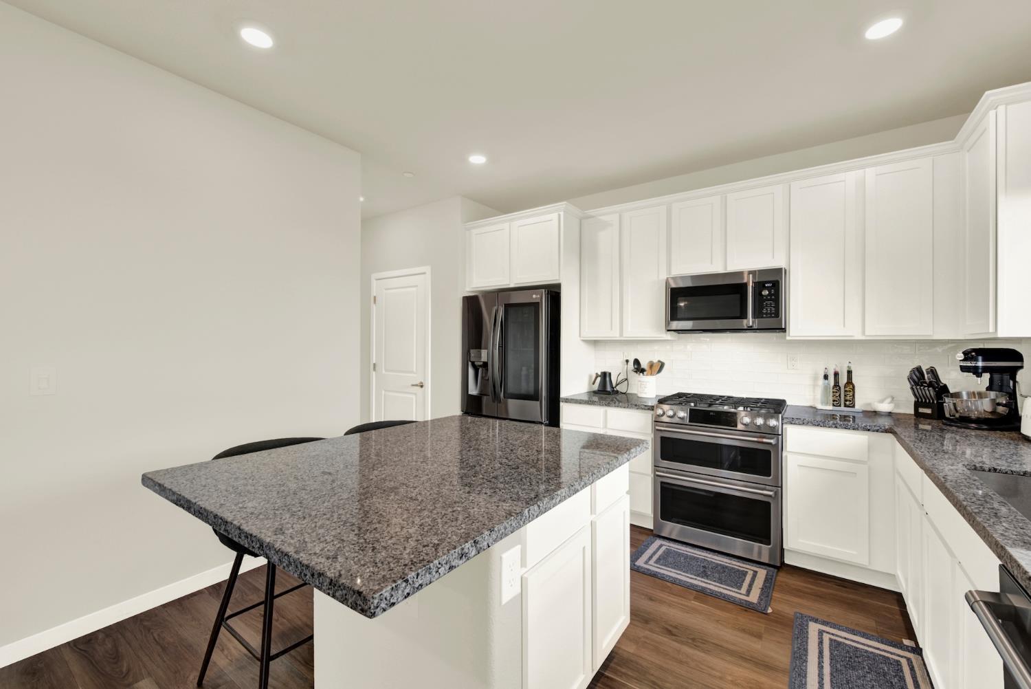 Kitchen with white cabinetry, a large granite island, and stainless steel appliances.