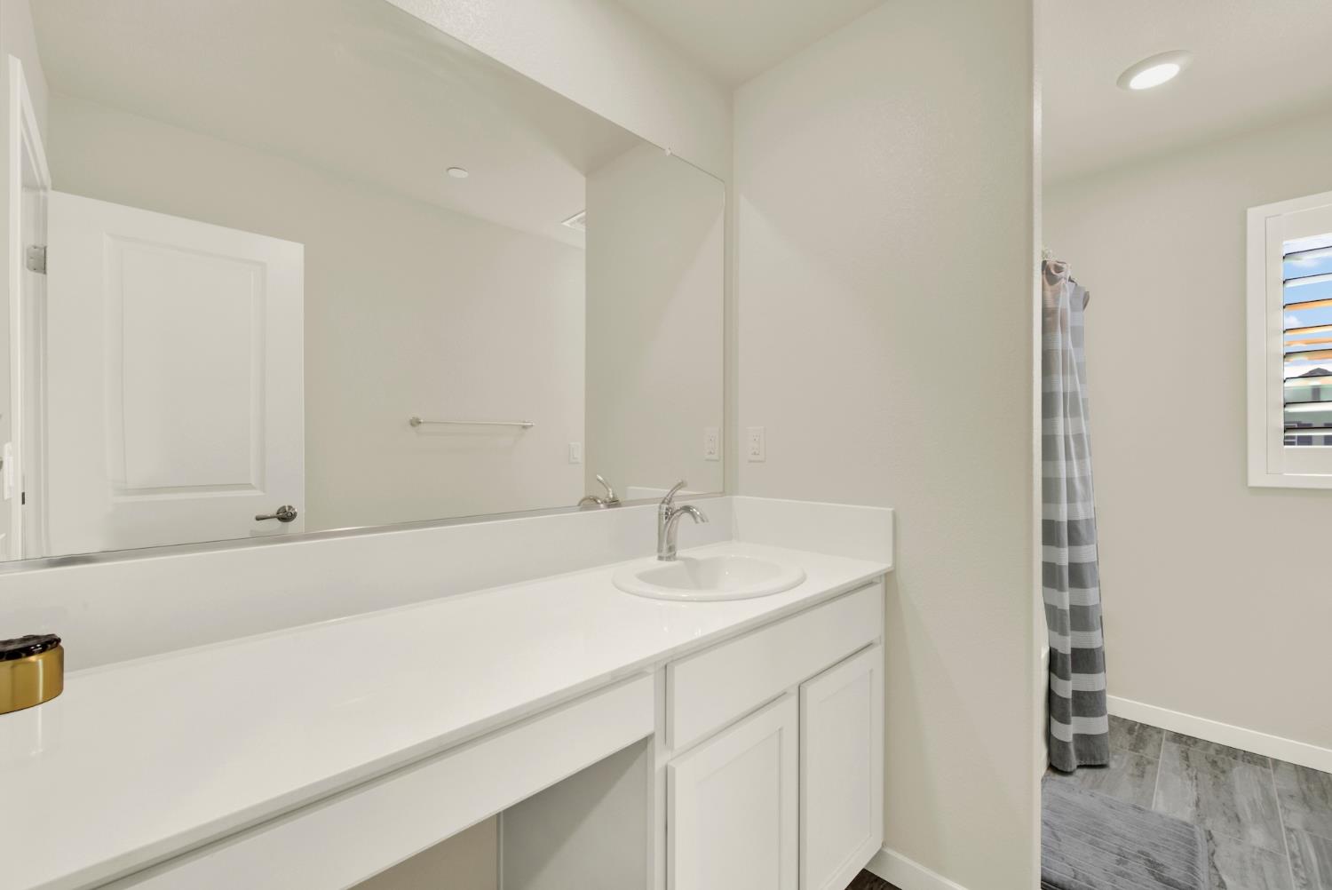Bathroom vanity with a long white counter, oval sink, large mirror, and gray striped shower curtain.