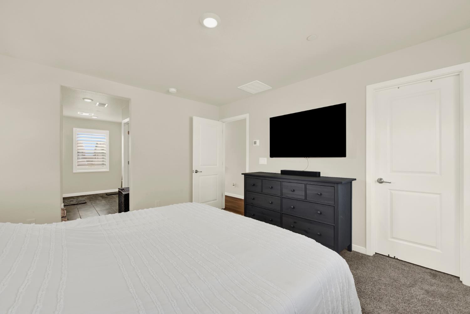 Bedroom with a white-covered bed, dark dresser, and wall-mounted television.