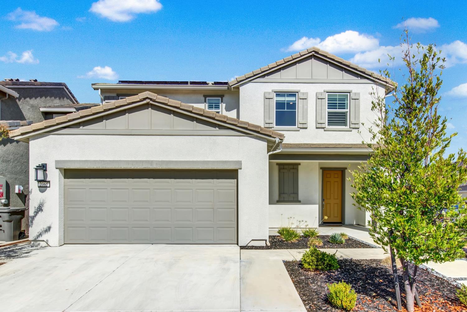 Two-story white stucco home with gray garage and trim, mustard-colored front door, and landscaped entry.