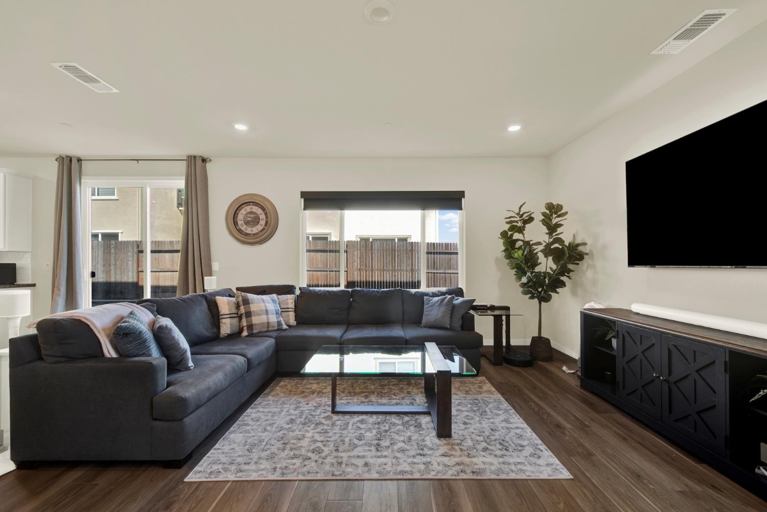 Living room with a dark sectional, glass coffee table, and windows facing a fenced yard.