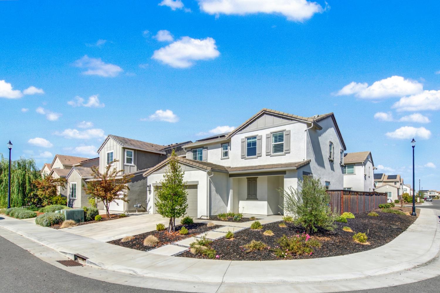 Two-story stucco home on a landscaped corner lot, with an attached garage and tiled roof.