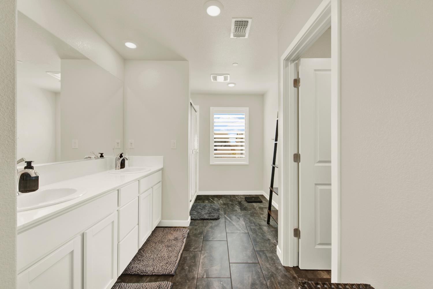Bathroom with a long double-sink vanity, dark tile floor, and shuttered window.