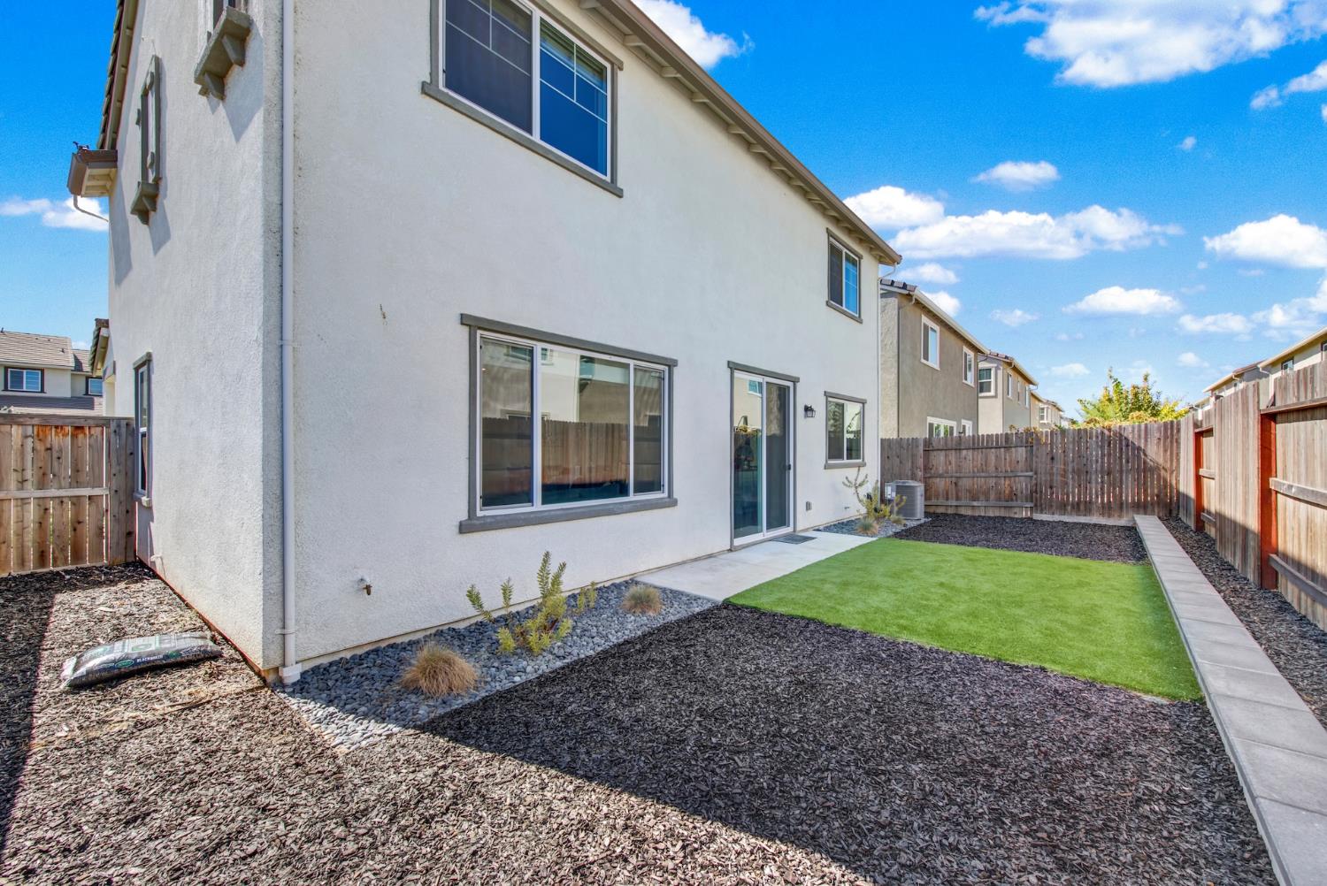 Rear exterior of a two-story home with fenced yard, artificial turf, and landscaped mulch beds.