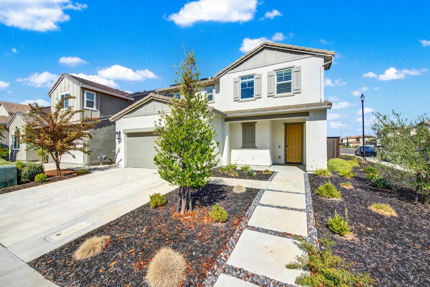 Two-story white stucco home with a tan front door, attached garage, and landscaped front yard.