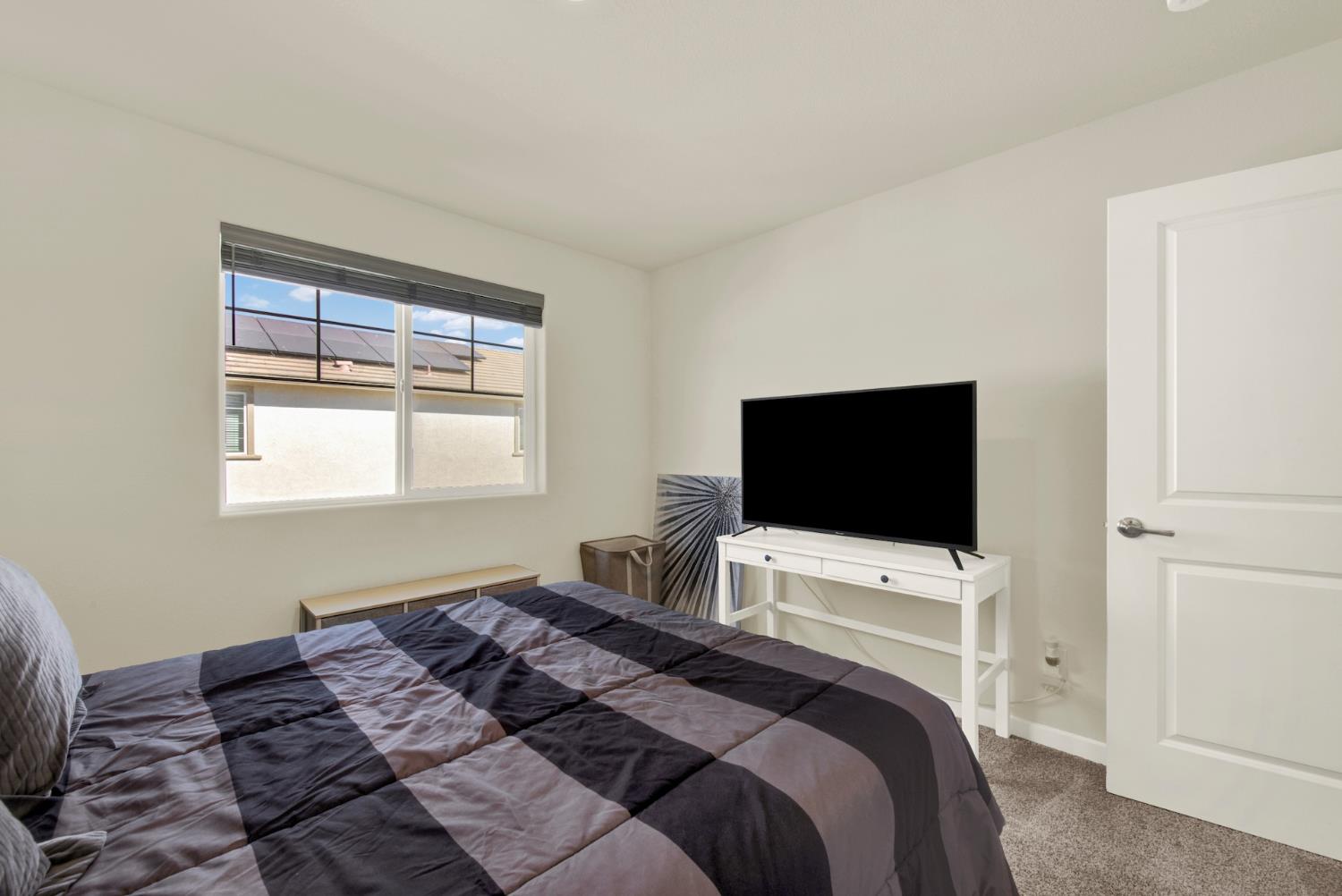 Bedroom with a gray-and-black striped bedspread, window with blinds, and television on a white console.