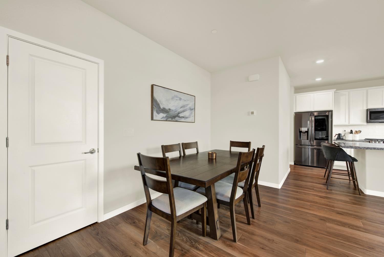 Dining area with a dark wood table and chairs beside a bright kitchen.