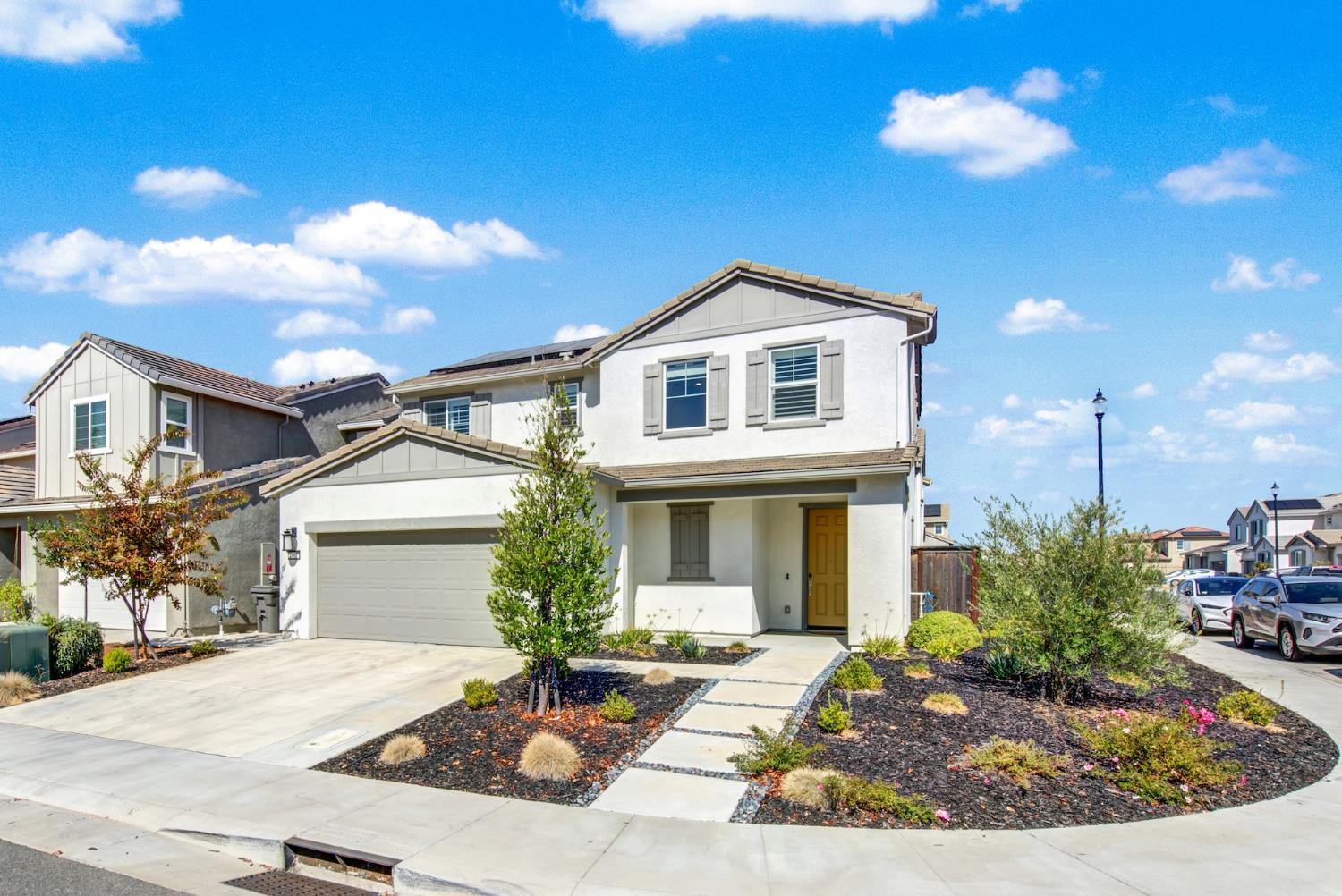 Two-story white house with an attached garage, mustard-yellow front door, and landscaped front yard.