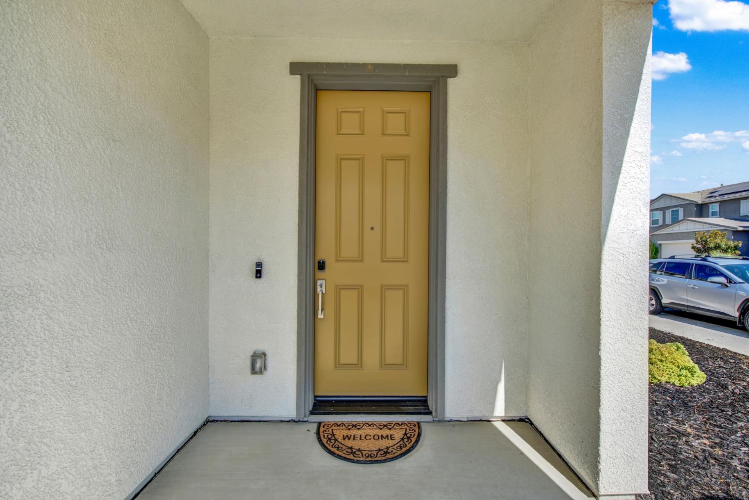 Covered entry with a mustard-yellow front door and a welcome mat.