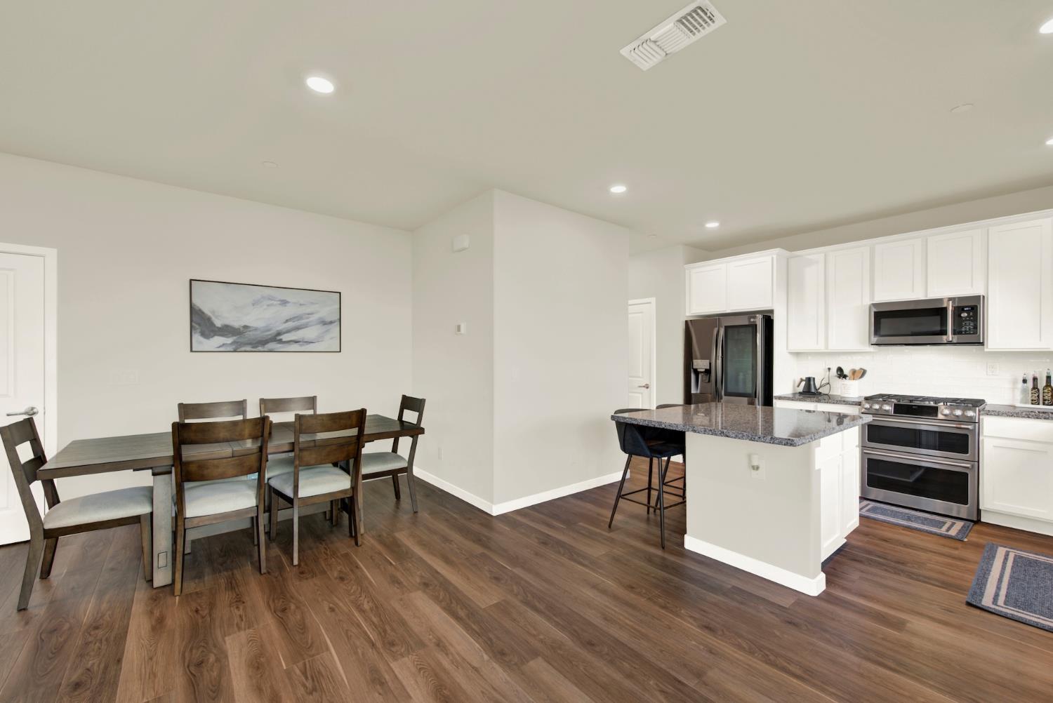 Open kitchen and dining area with a stone island, white cabinetry, and a dark wood dining table.