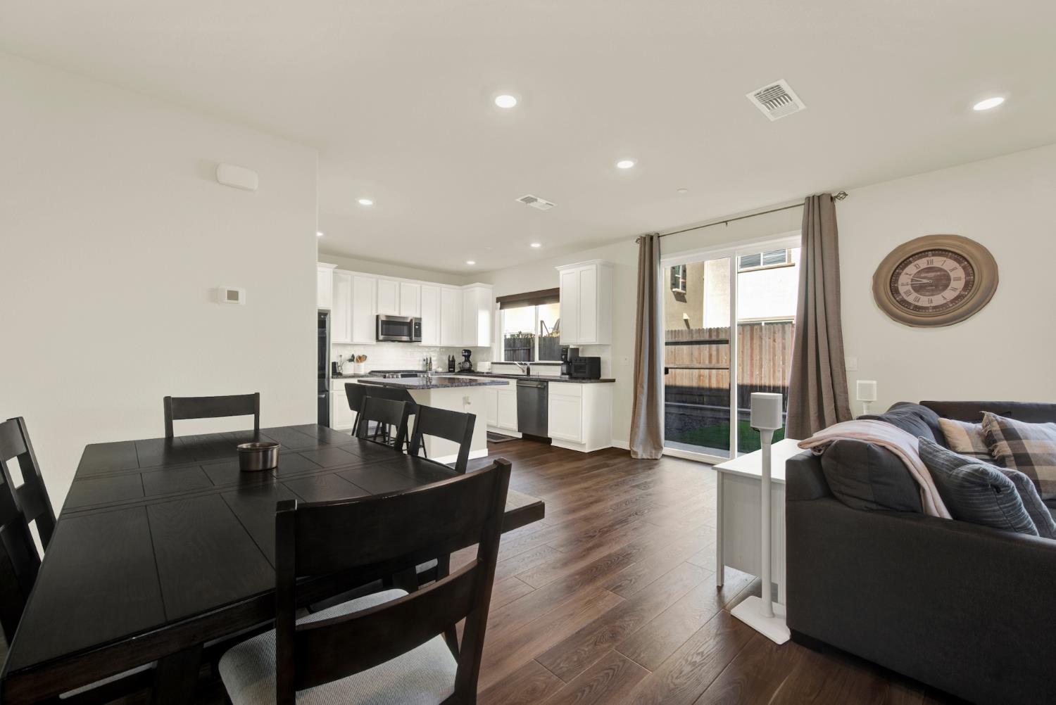 Open-plan dining, kitchen, and living area with white cabinets, dark wood-look floors, and a sliding glass door.