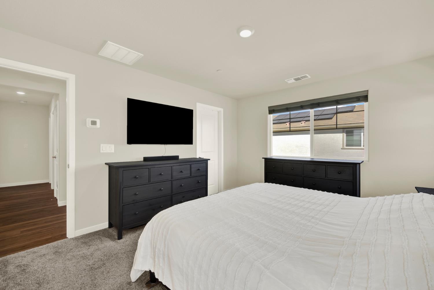 Bedroom with a white-covered bed, dark dressers, and a wall-mounted television.
