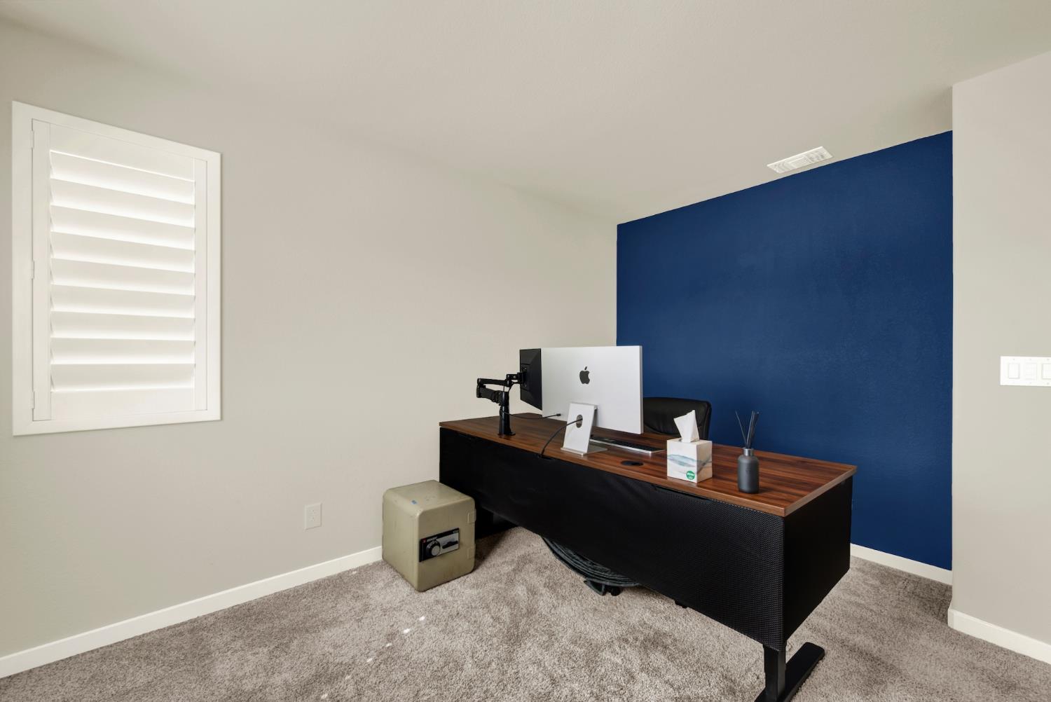 Home office with a blue accent wall, shuttered window, and wood-top desk.
