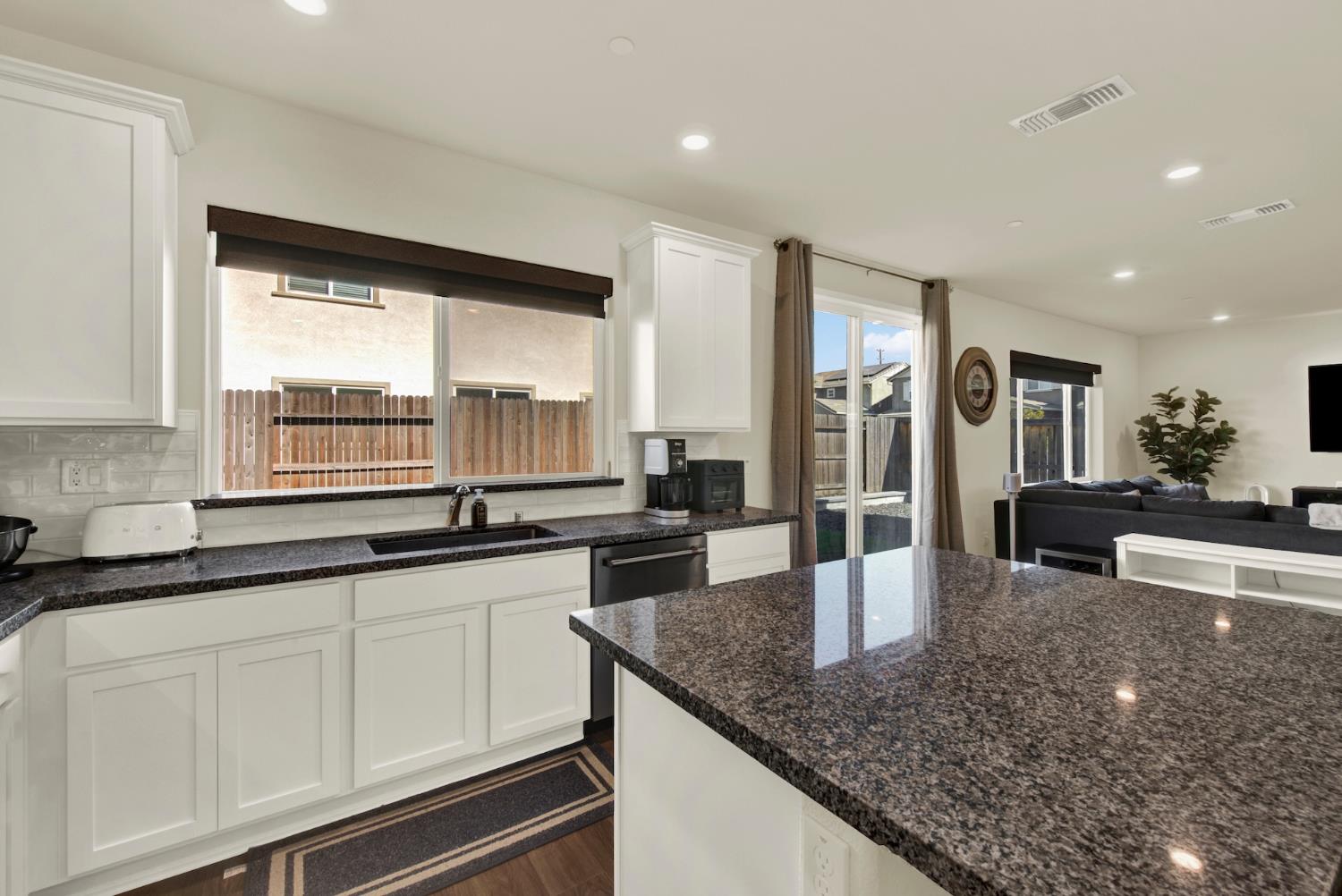 Kitchen with white cabinets, dark granite counters, and a large island opening to the living room.