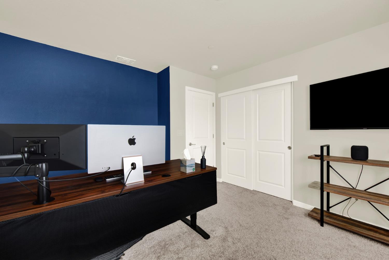 Home office with a large wood desk, blue accent wall, and wall-mounted television.