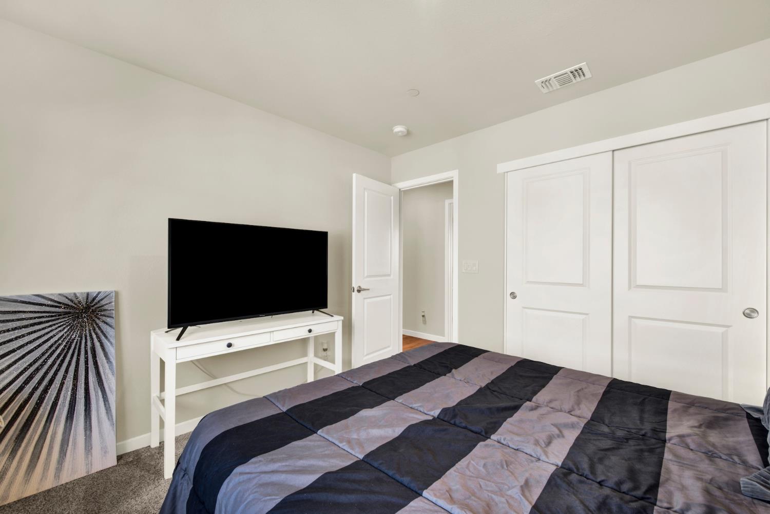 Bedroom with a patchwork quilt, television on a white console, and white closet doors.