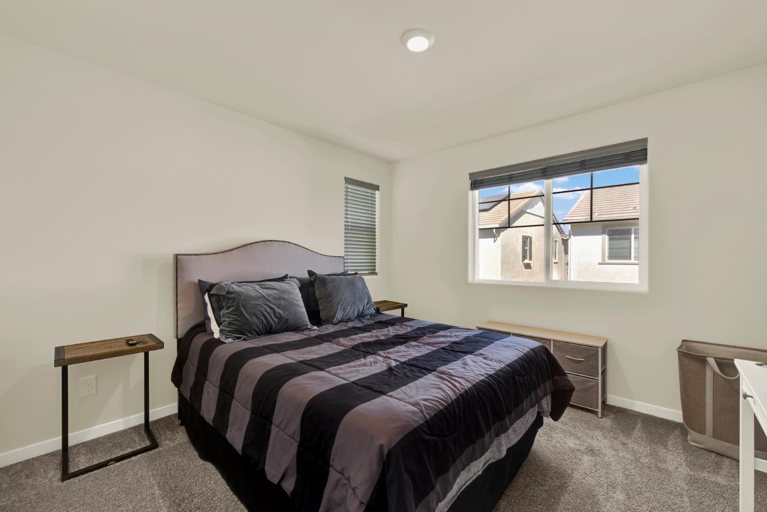 Bedroom with dark striped bedding, a light upholstered headboard, and a large window overlooking neighboring homes.