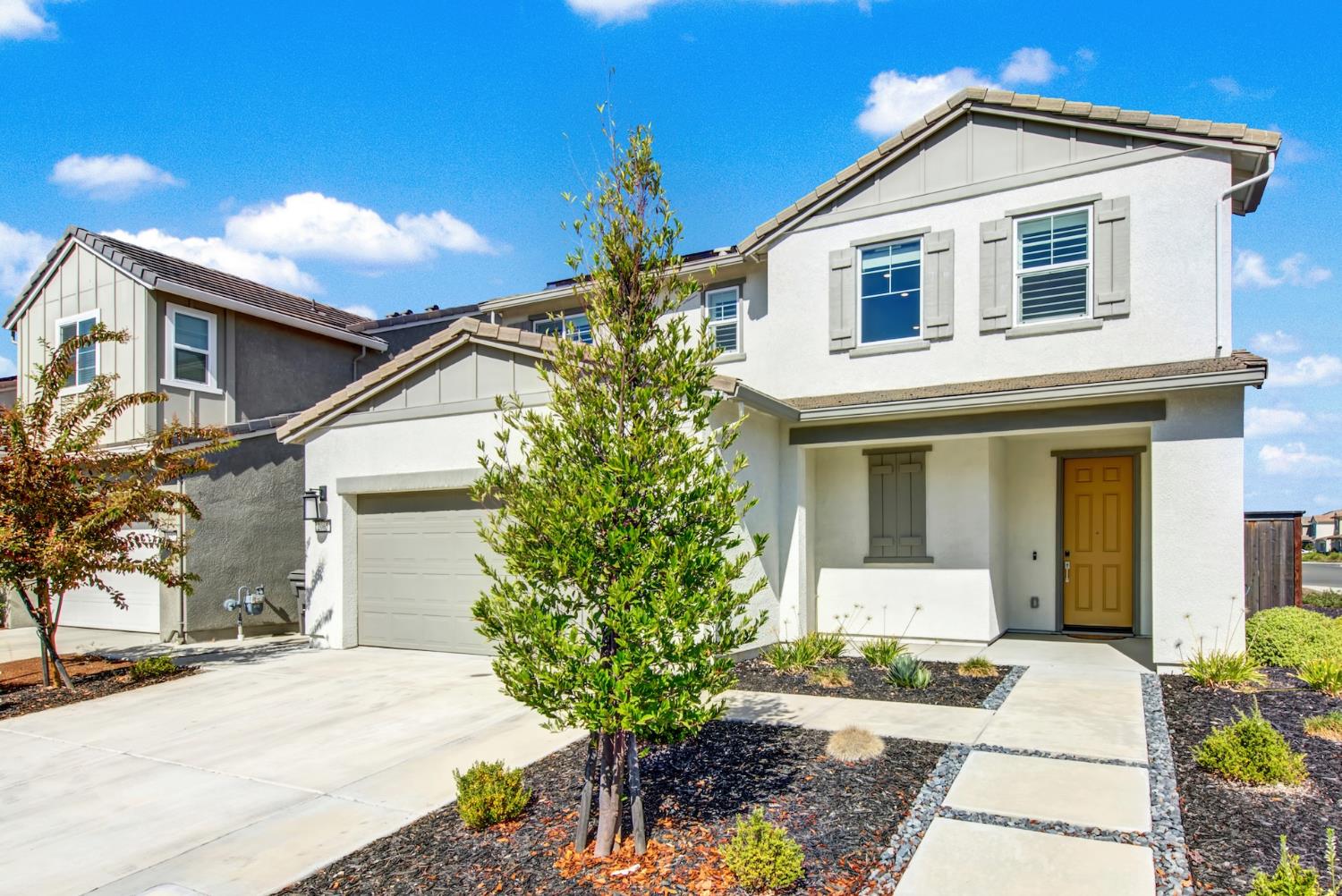 Two-story white stucco house with a yellow front door, attached garage, and landscaped walkway.