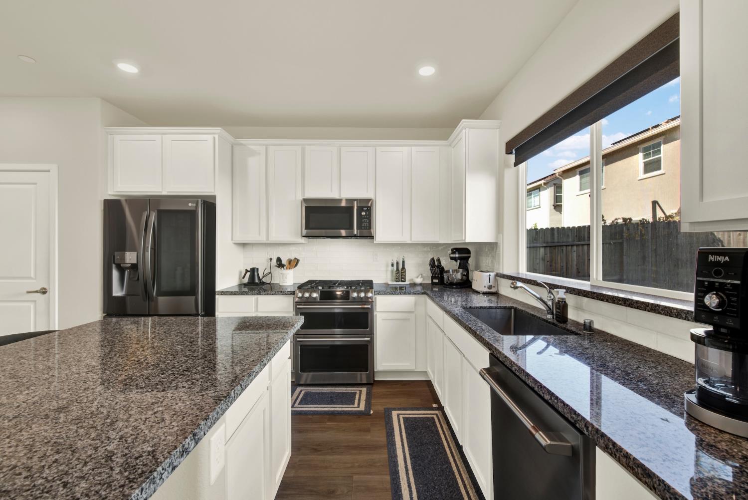 Kitchen with white cabinets, granite counters, a large island, and a wide window above the sink.