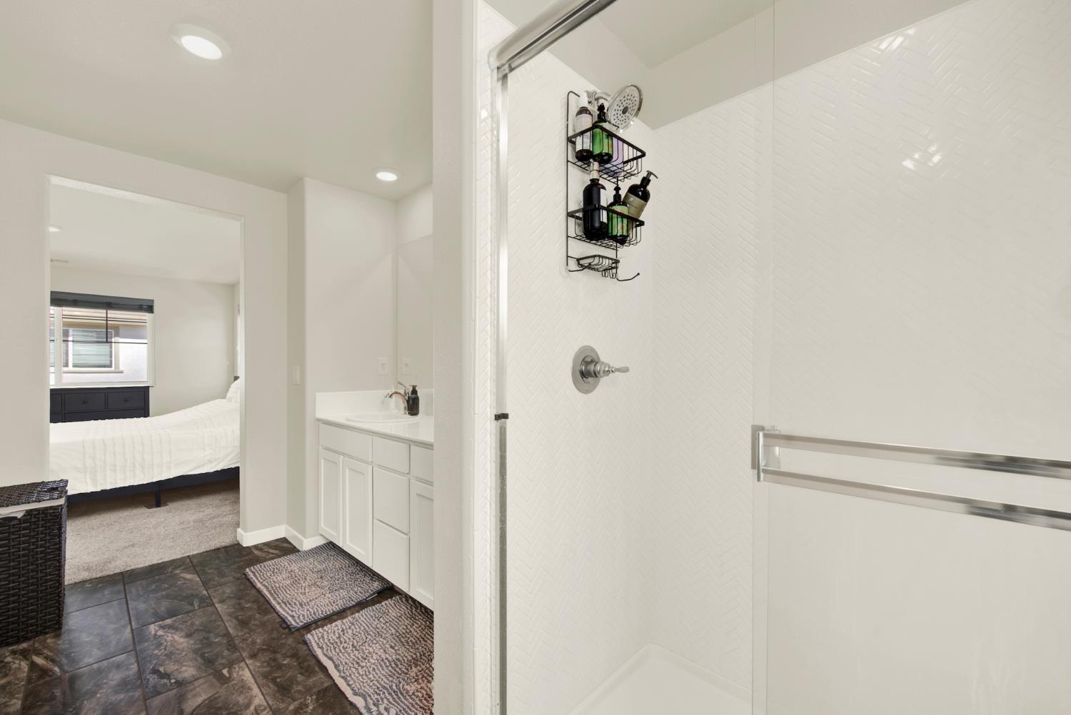 Bathroom with a white tiled walk-in shower and vanity, opening onto a bedroom.