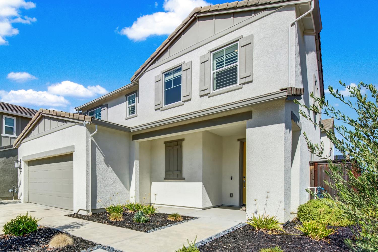 Two-story stucco house with an attached garage, covered entry, and landscaped front yard.