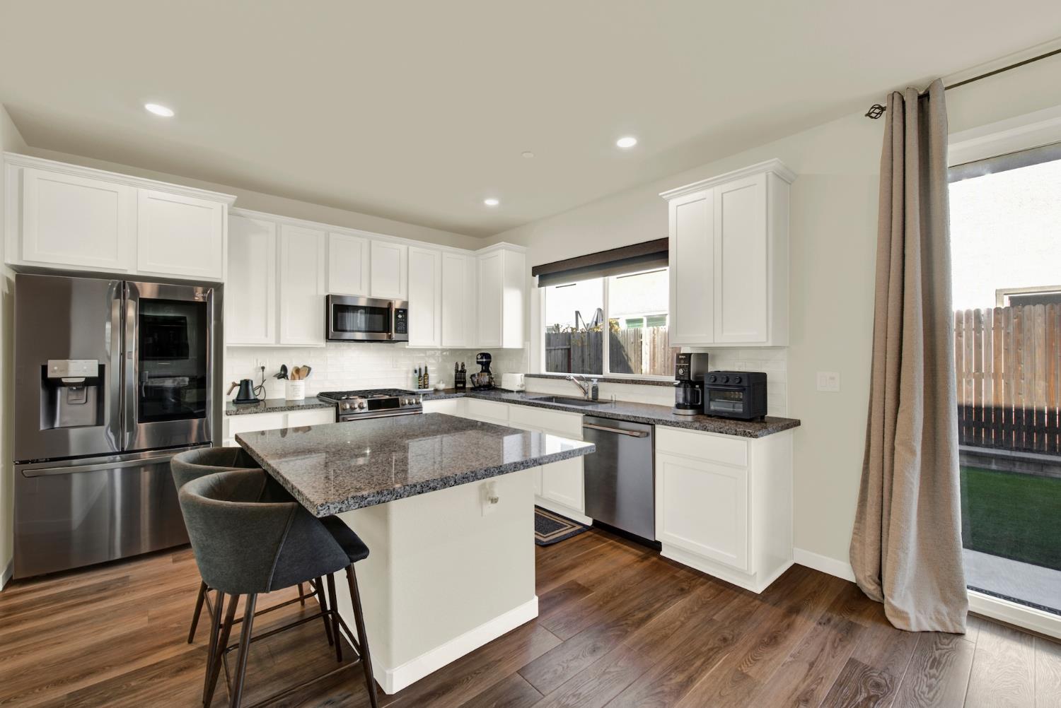Kitchen with white cabinets, granite island, stainless steel appliances, and sliding glass doors to the backyard.