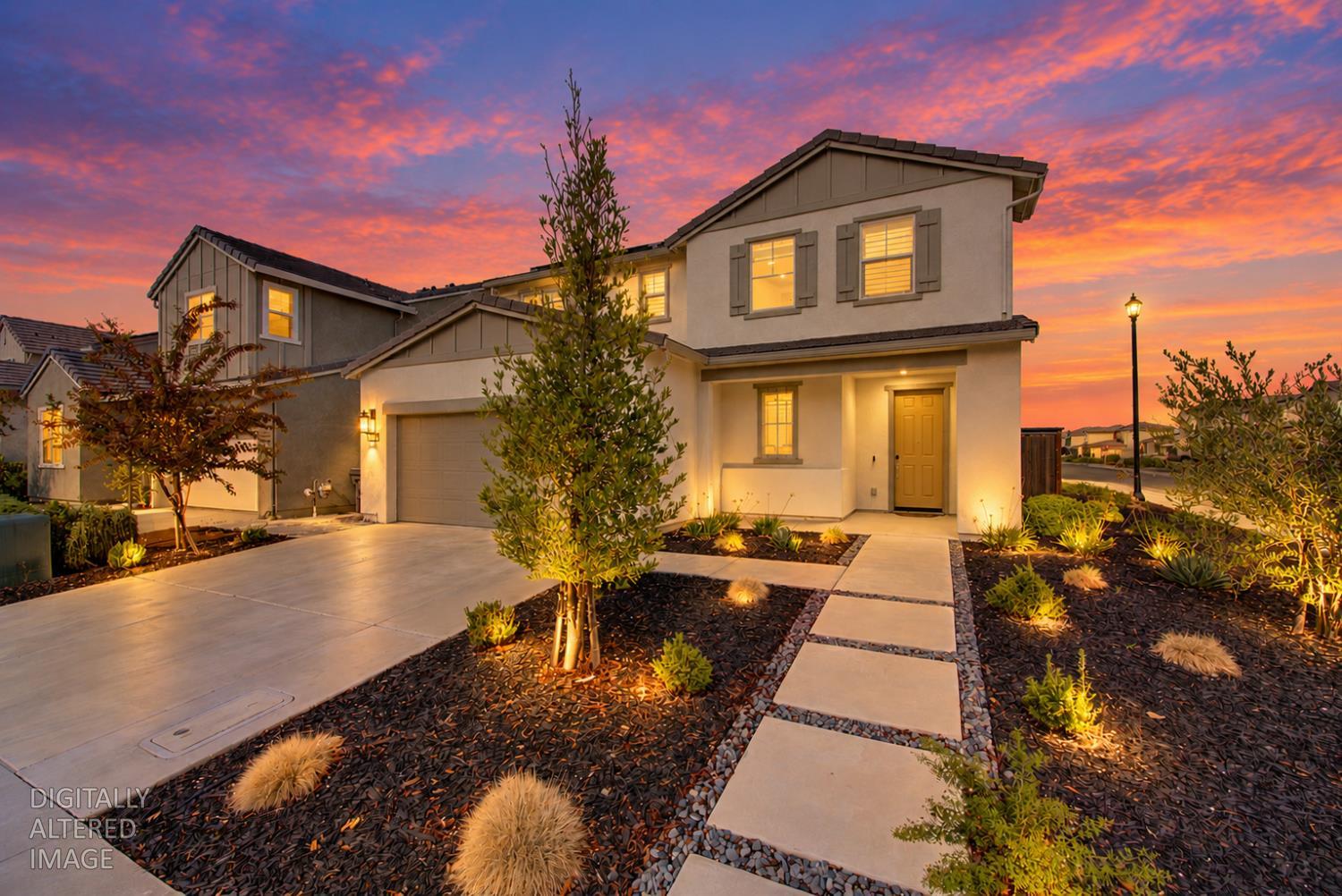 Two-story stucco home with a landscaped walkway and glowing windows at dusk.