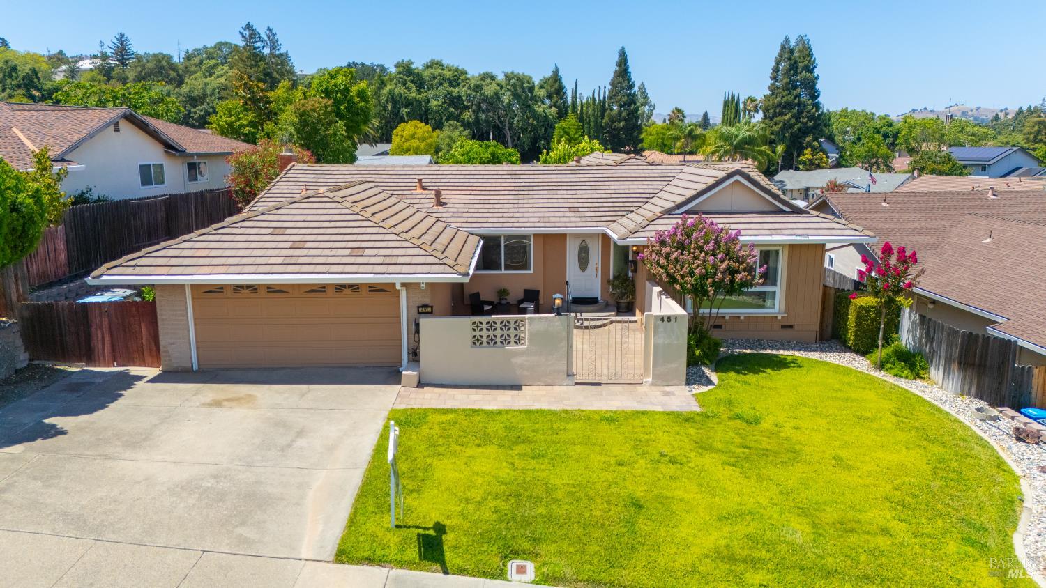 Single-story tan house with a tile roof, attached garage, and broad front lawn.