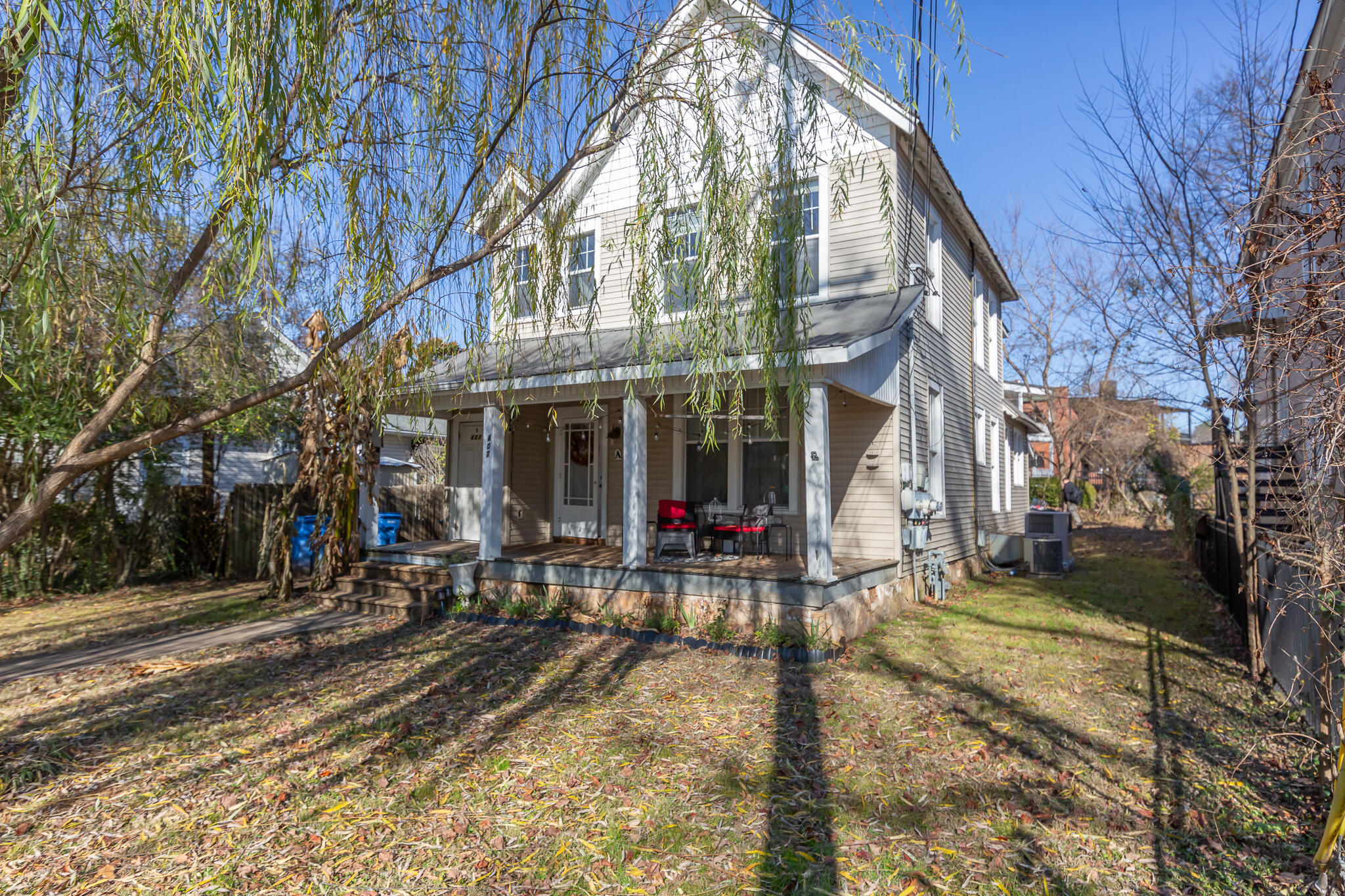 Two-story house with a covered porch, red chairs, and a leafy yard.