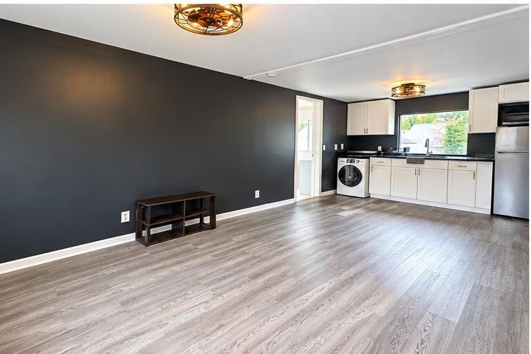 Open kitchen and living area with white cabinets, a front-loading washer, and gray wood-look flooring.