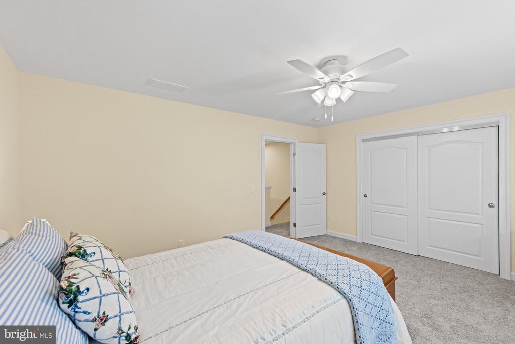 Bedroom with white bedding, blue patterned pillows, a ceiling fan, and double closet doors.
