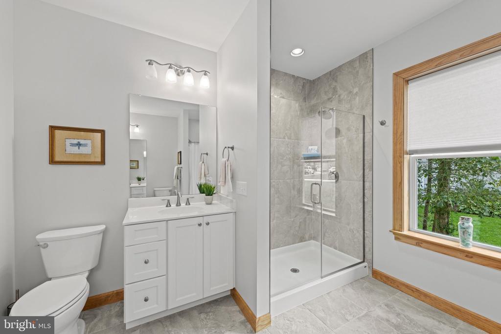 Bathroom with white vanity, glass-enclosed gray tile shower, and wood-trimmed window.