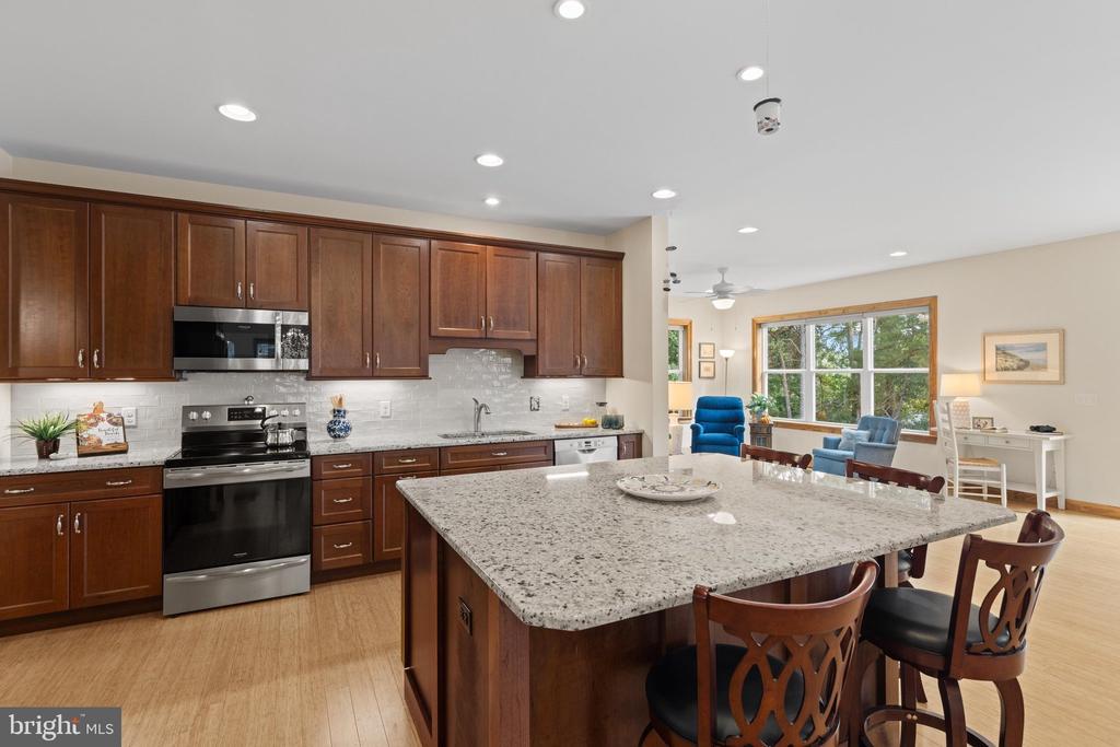 Kitchen with dark wood cabinets, stainless steel appliances, and a large granite island beside the living area.